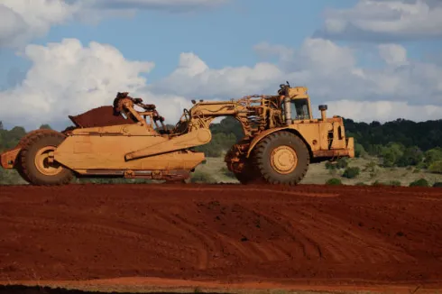 Large earthmoving scraper working on a red soil construction site, used for land leveling and soil preparation